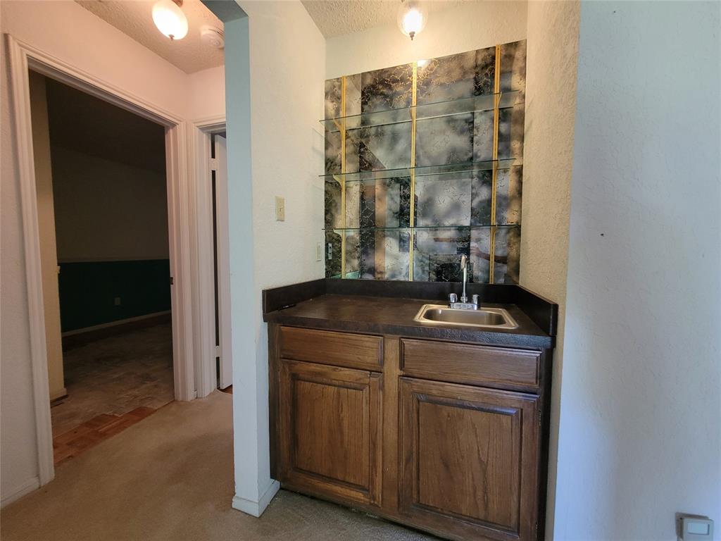 630 Country View Lane Garland, TX 75043 - Photo 7 of 29 Built-in wet bar featuring wood cabinetry, a stainless steel sink, dark countertop, and a decorative mirrored backsplash with glass shelving