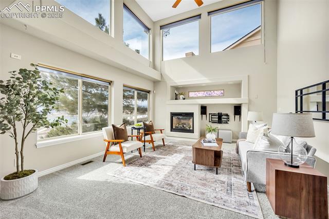 13884 Windy Oaks Road Colorado Springs, CO 80921 - Photo 3 of 21 Carpeted living room with a glass covered fireplace, a ceiling fan, a high ceiling, and baseboards