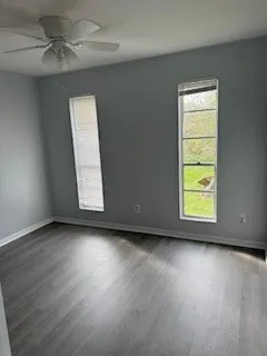 an empty room with wooden floor chandelier fan and windows