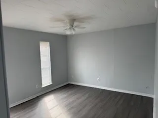 an empty room with wooden floor fan and windows