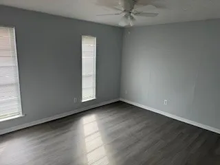 an empty room with wooden floor fan and windows