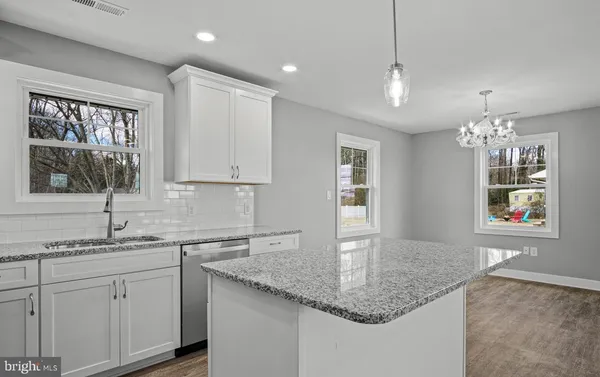 a kitchen with stainless steel appliances granite countertop a sink dishwasher and white cabinets with wooden floor