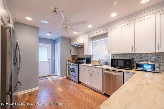 a kitchen with stainless steel appliances granite countertop a refrigerator a stove and a sink with wooden floor