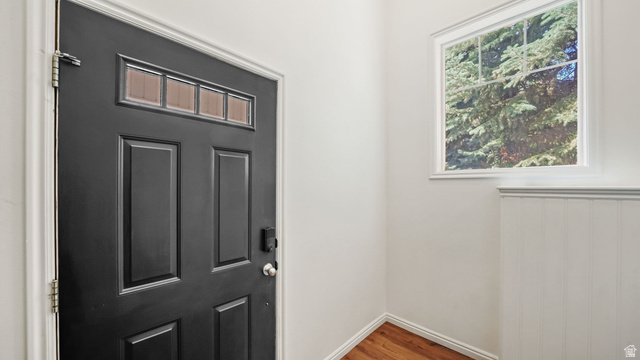 Black paneled door with transom window, white walls, beadboard wainscoting, and wood-finish flooring