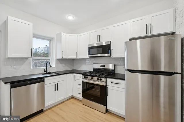 a white kitchen with stainless steel appliances a refrigerator a sink and white cabinets