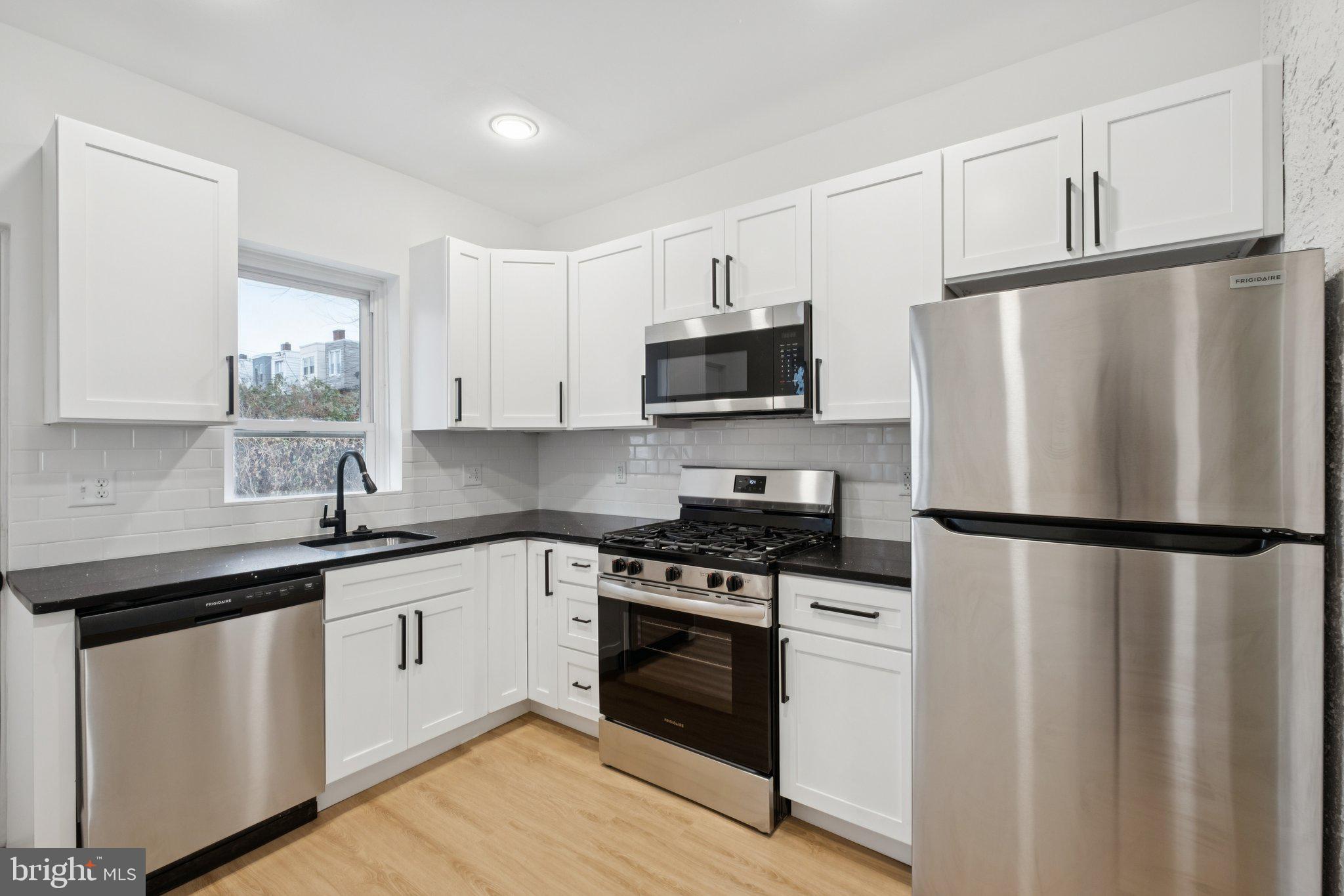 a white kitchen with stainless steel appliances a refrigerator a sink and white cabinets