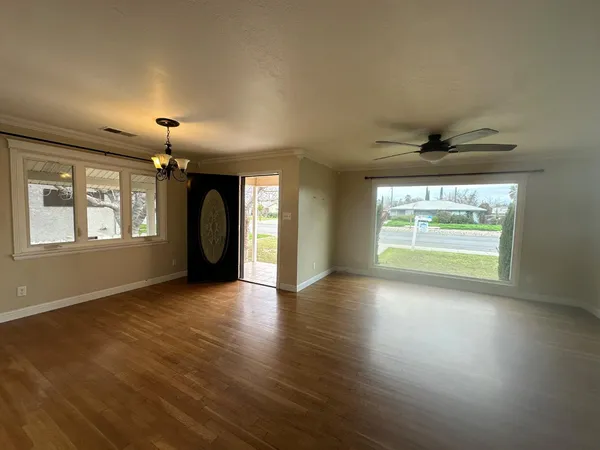an empty room with wooden floor chandelier and windows
