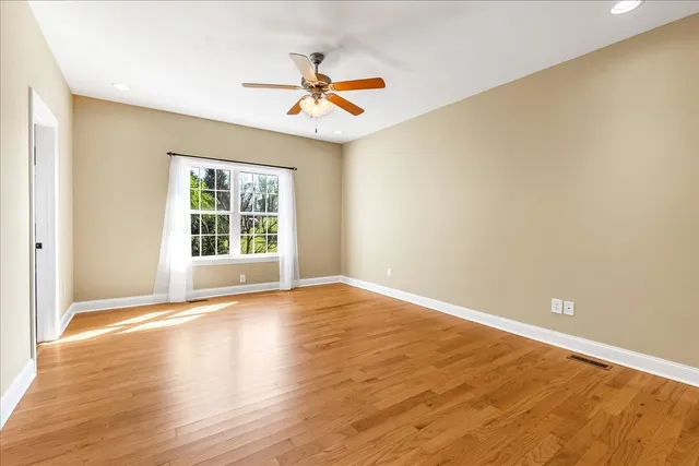 an empty room with wooden floor fan and windows