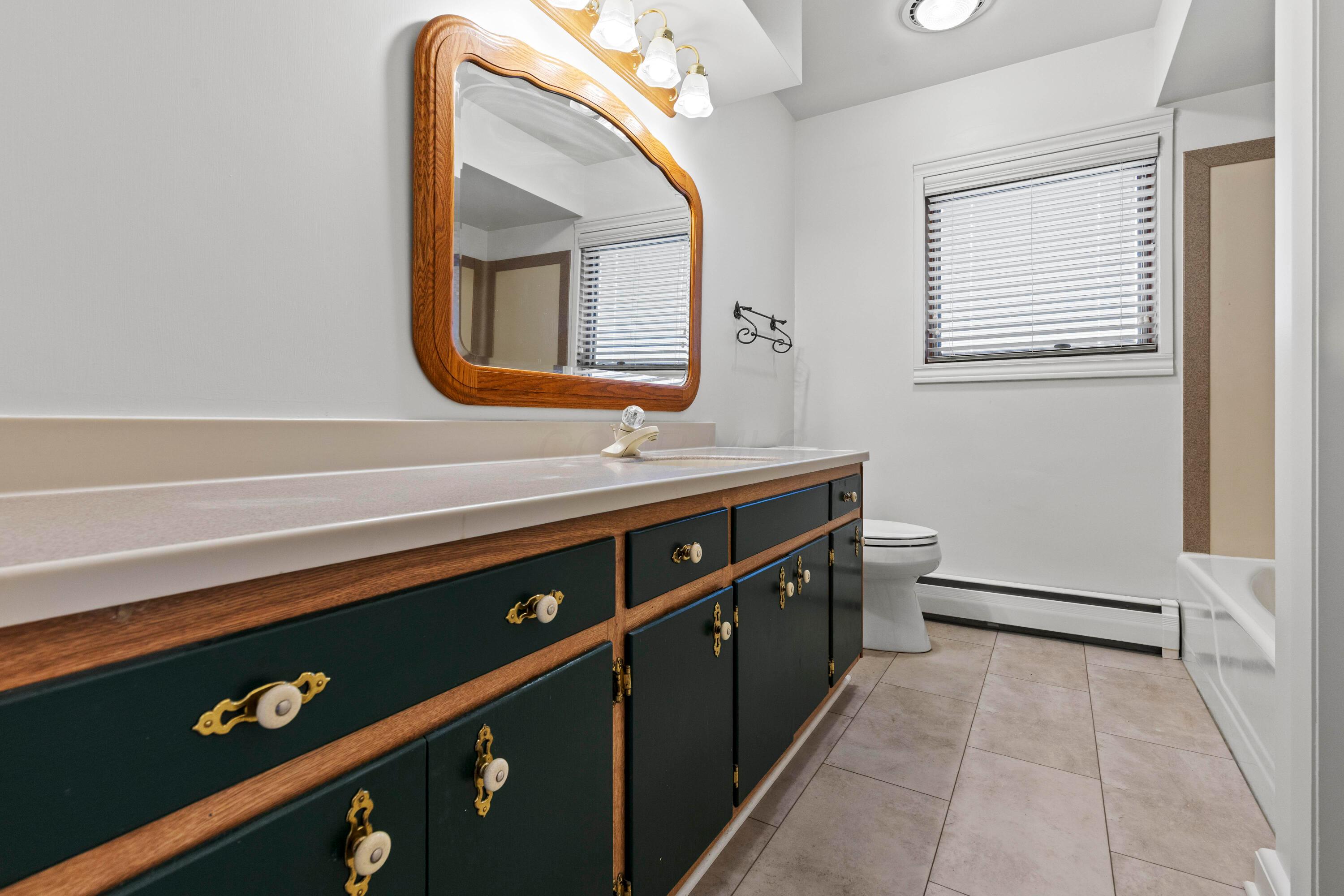 6982 Lee Road Westerville, OH 43081 - Photo 38 of 71 • New grouted vinyl flooring ~ 2024 • White painted walls • Tub/shower combination with corian surround • 4 bulb wall light • Linen closet with bi-fold doors