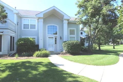 a view of a brick house with a yard plants and large tree
