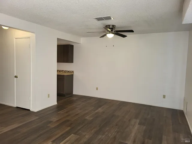 a view of an empty room with wooden floor and a ceiling fan