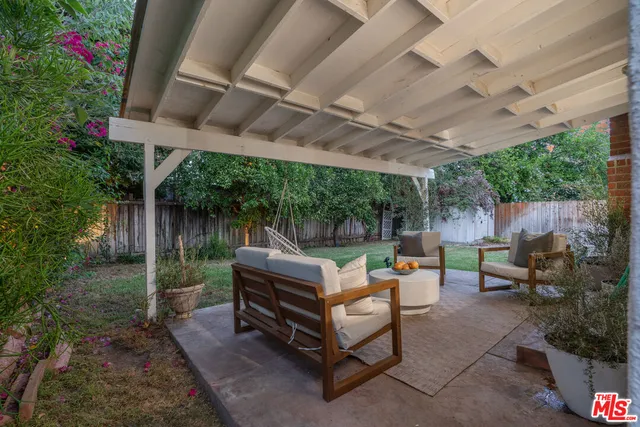 a view of a backyard with table and chairs and couches with wooden fence and plants