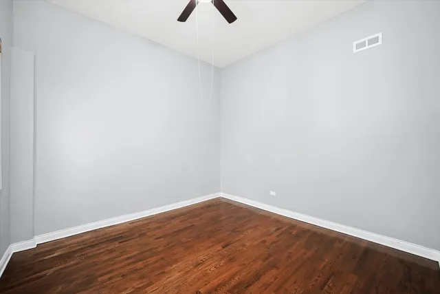 a view of an empty room with wooden floor and a ceiling fan