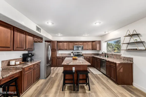 a kitchen with stainless steel appliances granite countertop a stove top oven a sink dishwasher a dining table and chairs with wooden floor