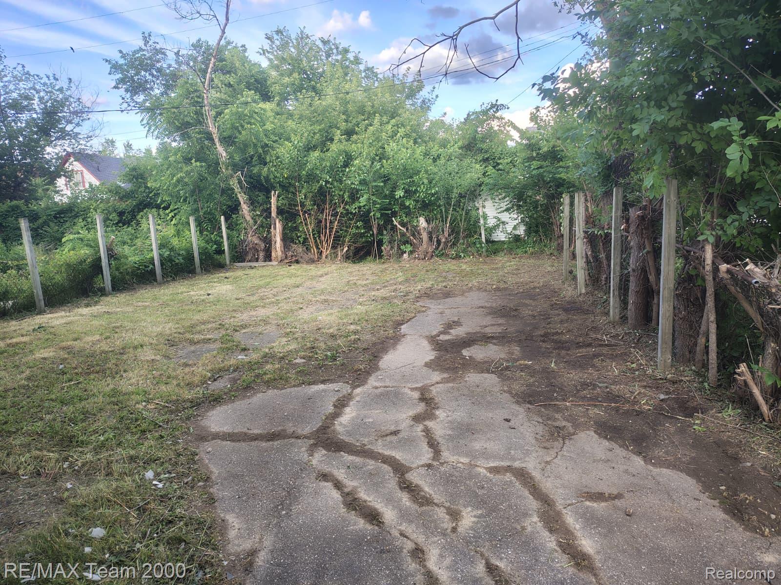 8860 Appoline Street Detroit, MI 48228 - Photo 4 of 45 Expansive lot featuring a concrete path, perimeter fencing, mature trees, and natural greenery