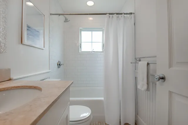 a bathroom with a granite countertop bathtub shower sink vanity and toilet