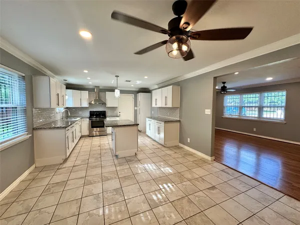 a large white kitchen with kitchen island a stove a sink dishwasher and white cabinets with wooden floor
