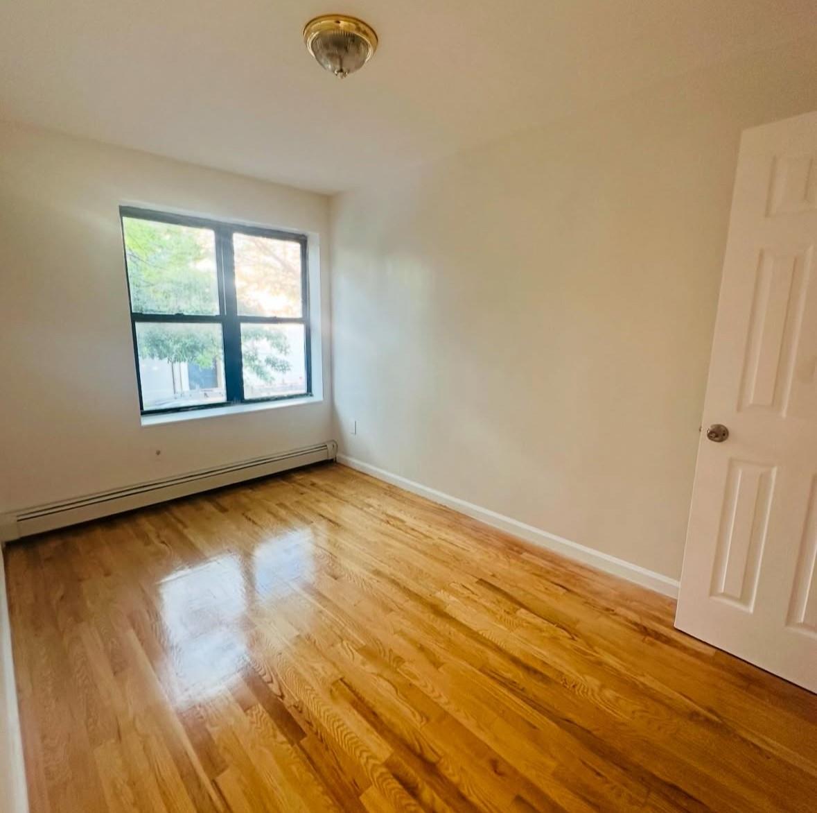 1079 Willoughby Avenue Brooklyn, NY 11221 - Photo 4 of 19 Empty room featuring a baseboard radiator and light hardwood / wood-style flooring