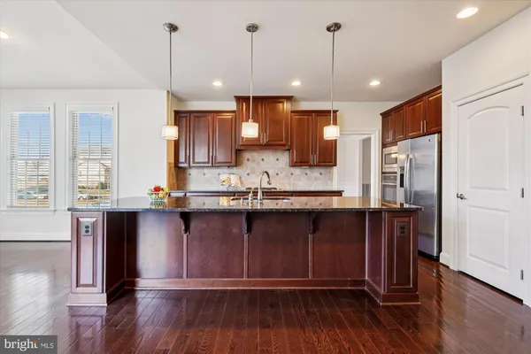a open kitchen with stainless steel appliances granite countertop wooden floors wooden cabinets a sink and a window