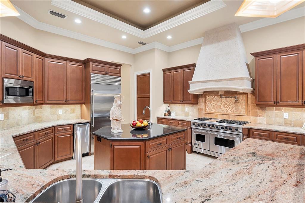 7007 Portmarnock Place Lakewood Ranch, FL 34202 - Photo 22 of 92 a kitchen with stainless steel appliances granite countertop a stove top oven a sink dishwasher a dining table and chairs with wooden floor