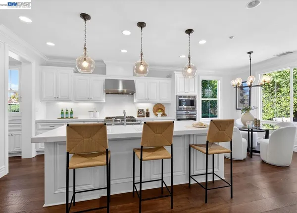 a kitchen with stainless steel appliances granite countertop a stove a refrigerator a kitchen island a dining table and chairs with wooden floor