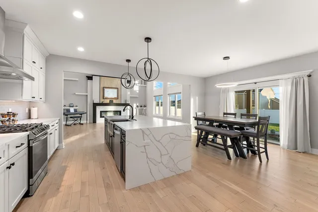 a kitchen with stainless steel appliances granite countertop a stove top oven a sink dishwasher a dining table and chairs with wooden floor