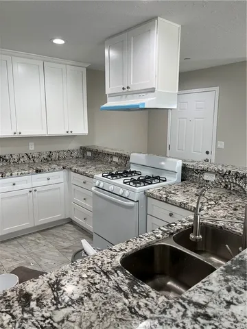 a kitchen with granite countertop a sink a stove and cabinets