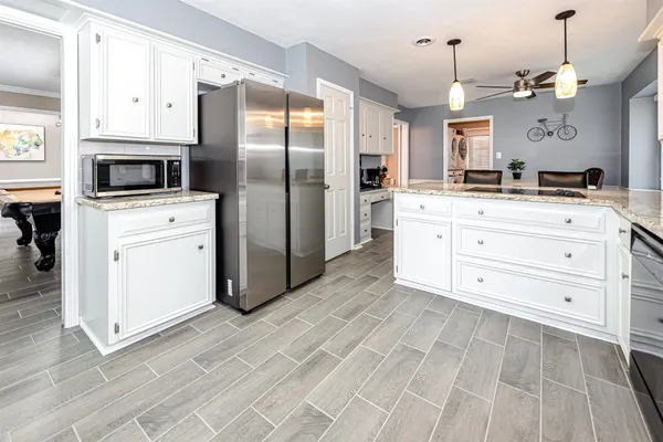 a kitchen with stainless steel appliances kitchen island granite countertop a refrigerator a oven and white cabinets with wooden floor