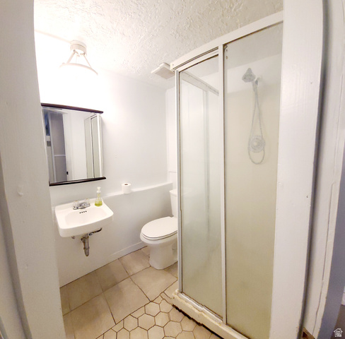 684 East 400 North Logan, UT 84321 - Photo 26 of 27 Compact bathroom featuring a wall-mounted sink with chrome faucet, a white toilet, and a glass-enclosed shower with a handheld showerhead