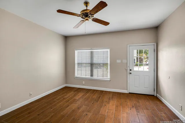 an empty room with wooden floor chandelier fan and windows