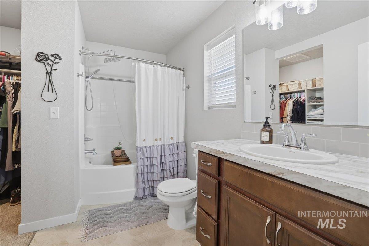 16682 Loggia Avenue Caldwell, ID 83607 - Photo 26 of 46 Bathroom featuring a walk in closet, vanity, shower / bath combo with shower curtain, decorative backsplash, and suspended lighting