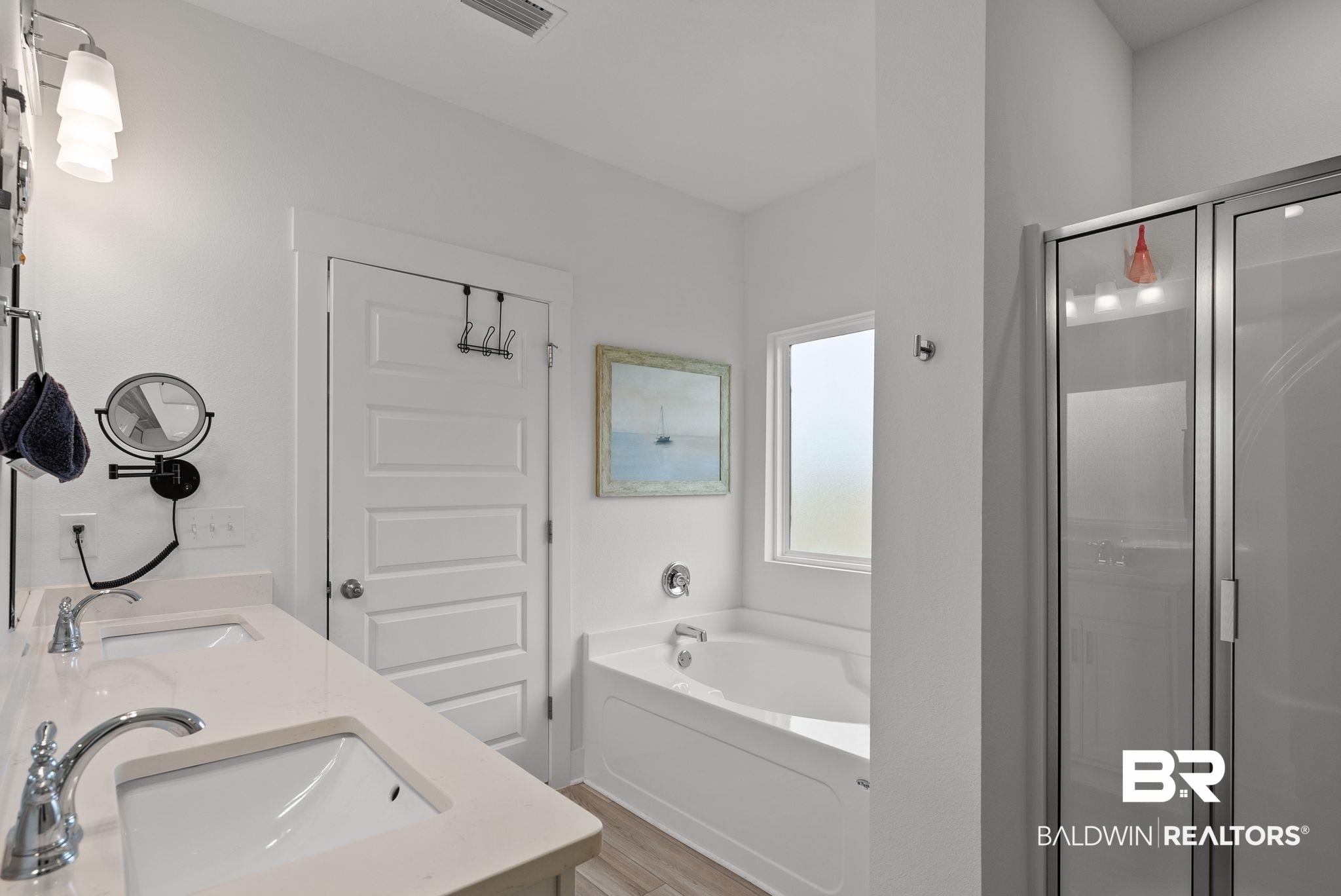 9899 Willet Way Foley, AL 36535 - Photo 21 of 37 Contemporary bathroom featuring a dual vanity with light-toned countertops and undermount sinks, a built-in soaking tub, a separate glass-enclosed shower, and wood-finish flooring