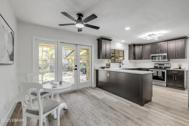 a kitchen with stainless steel appliances kitchen island granite countertop a refrigerator a stove top oven a sink a dining table and chairs with wooden floor