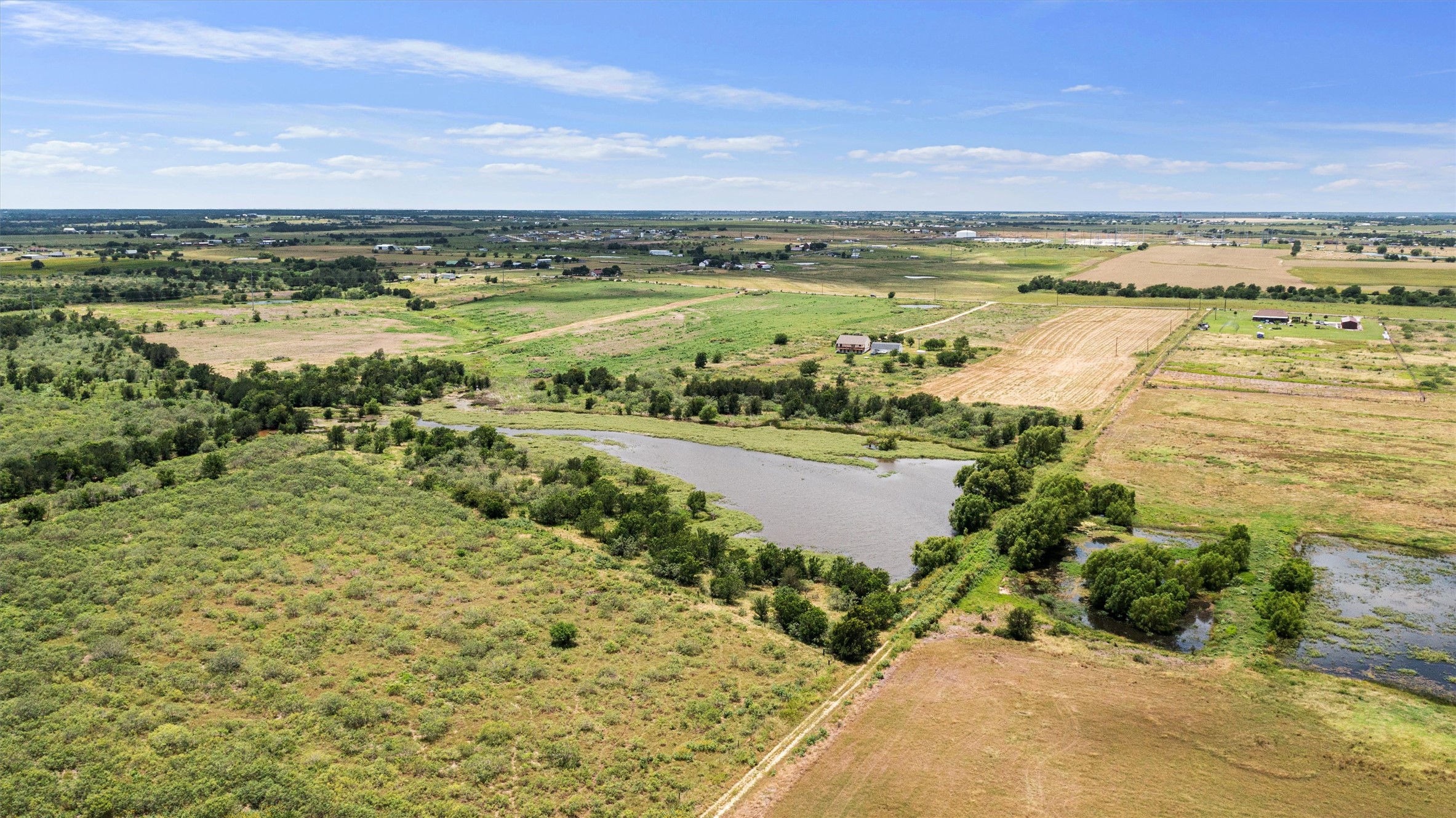 3315 County Road 463 Elgin, TX 78621 - Photo 30 of 32 Acres of verdant land unfold, featuring a tranquil pond and distant structures under an open sky.
