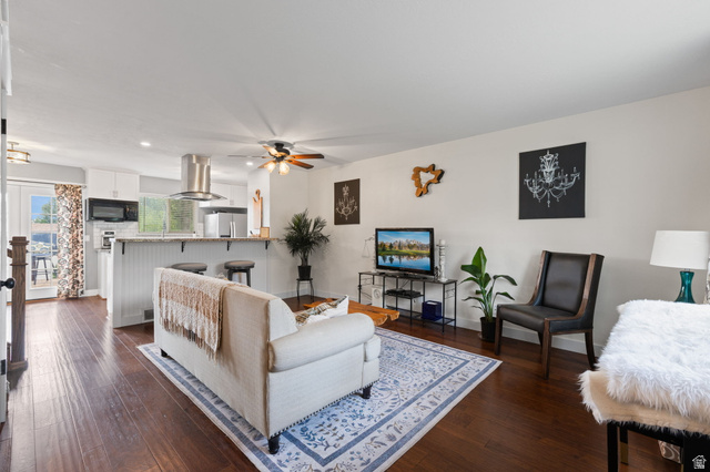 Open-concept living area featuring rich wood-finish flooring, a ceiling fan, recessed lighting, and a white kitchen with stainless steel appliances