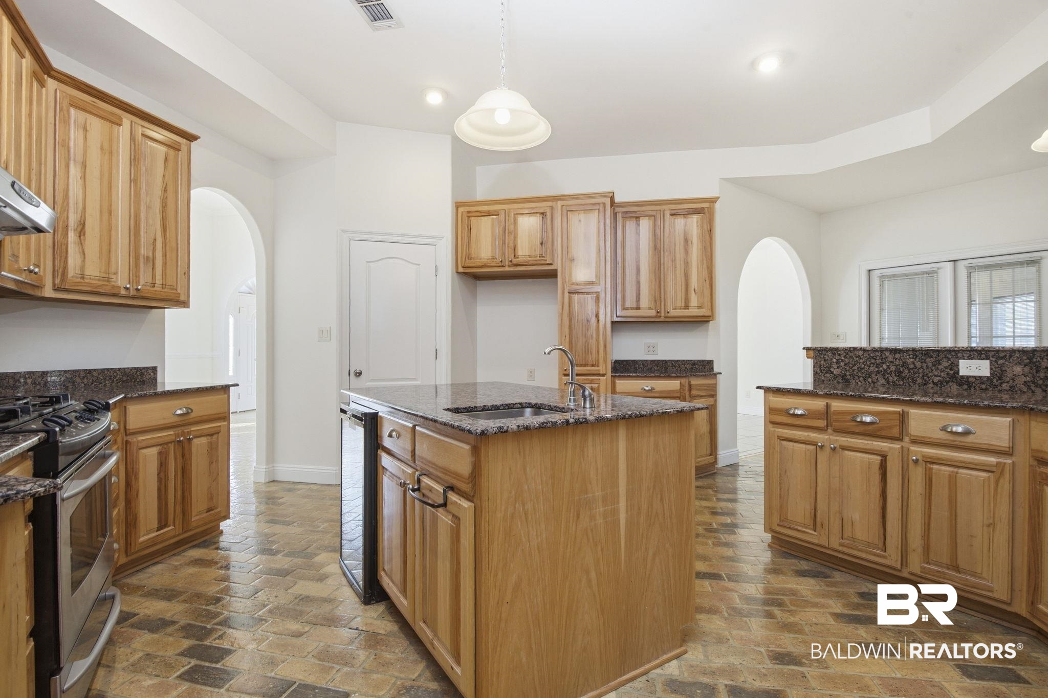 29634 St George Street Daphne, AL 36526 - Photo 20 of 47 Kitchen with arched walkways, dark stone counters, a center island with sink, and stainless steel range with gas cooktop