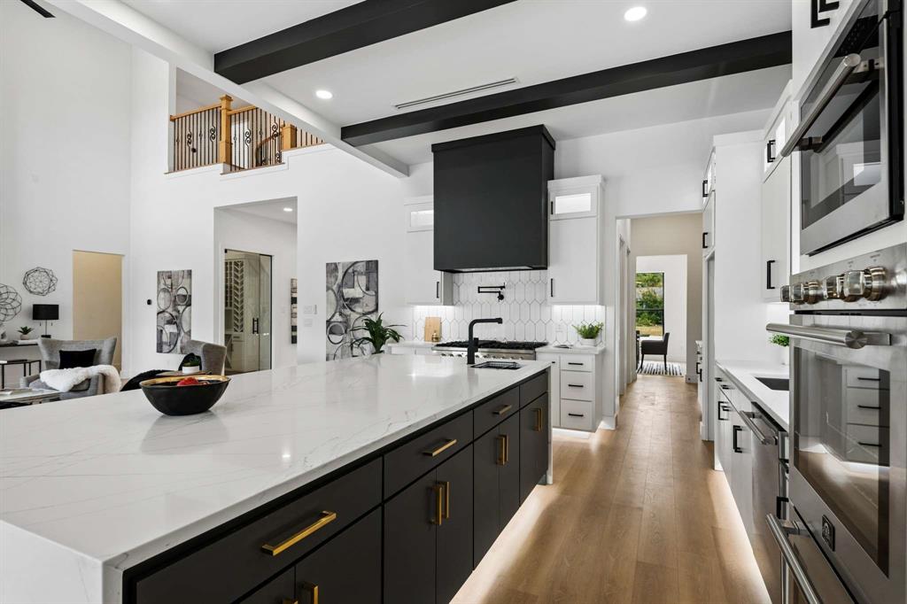 6606 Curtis Road Colleyville, TX 76034 - Photo 13 of 39 Expansive kitchen featuring a large island with white countertops, stainless steel appliances, wood-finish flooring, and exposed ceiling beams