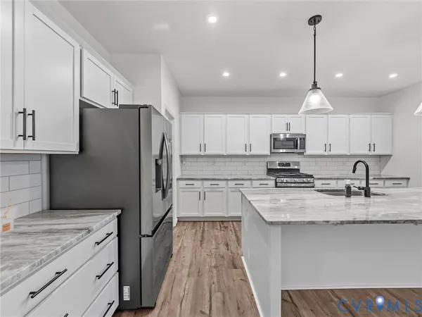 a kitchen with stainless steel appliances granite countertop a refrigerator a sink dishwasher a stove and white cabinets with wooden floor