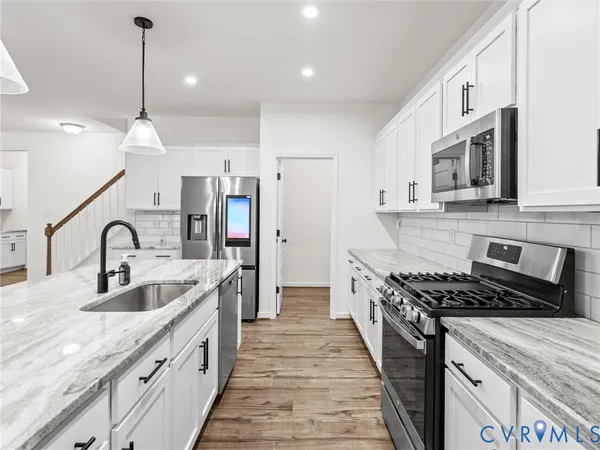 a kitchen with stainless steel appliances granite countertop a sink stove a refrigerator a kitchen island with white cabinets and wooden floor