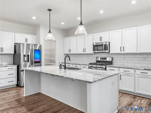 a kitchen with stainless steel appliances granite countertop a sink a stove a refrigerator and white cabinets with wooden floor