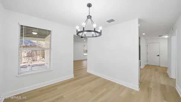 a view of a room with wooden floor chandeliers and kitchen view