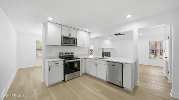 a kitchen with stainless steel appliances granite countertop a stove top oven a sink a refrigerator and white cabinets with wooden floor