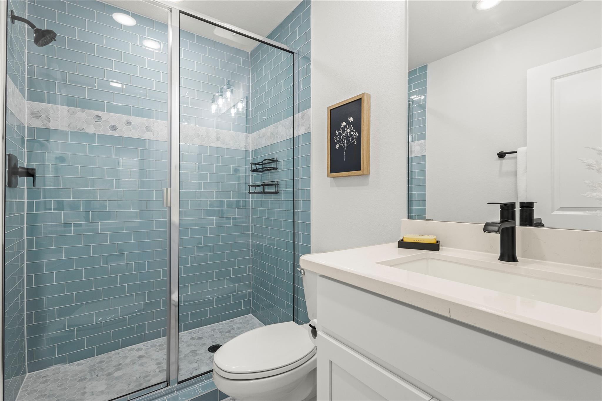 1128 Villa Rialto View Leander, TX 78641 - Photo 33 of 40 A striking glass-enclosed shower boasts serene blue subway tiles, creating a tranquil bathroom retreat.