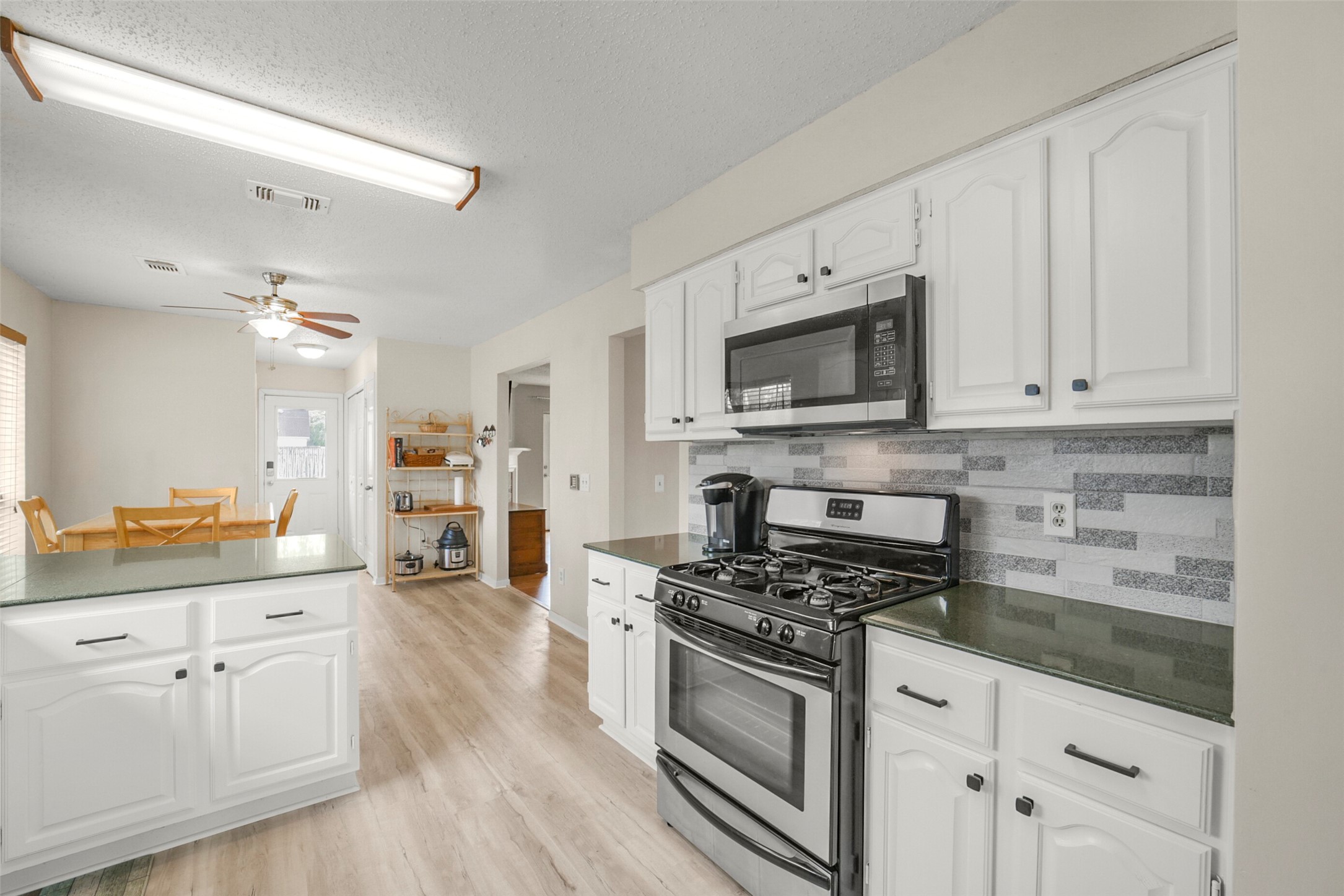 10410 Dude Road Houston, TX 77064 - Photo 1 of 45 Bright and modern kitchen with white cabinetry, stainless steel appliances, and a stylish tile backsplash. It features a gas stove, microwave, and ample counter space. An adjacent dining area with natural light offers a cozy space for meals.
