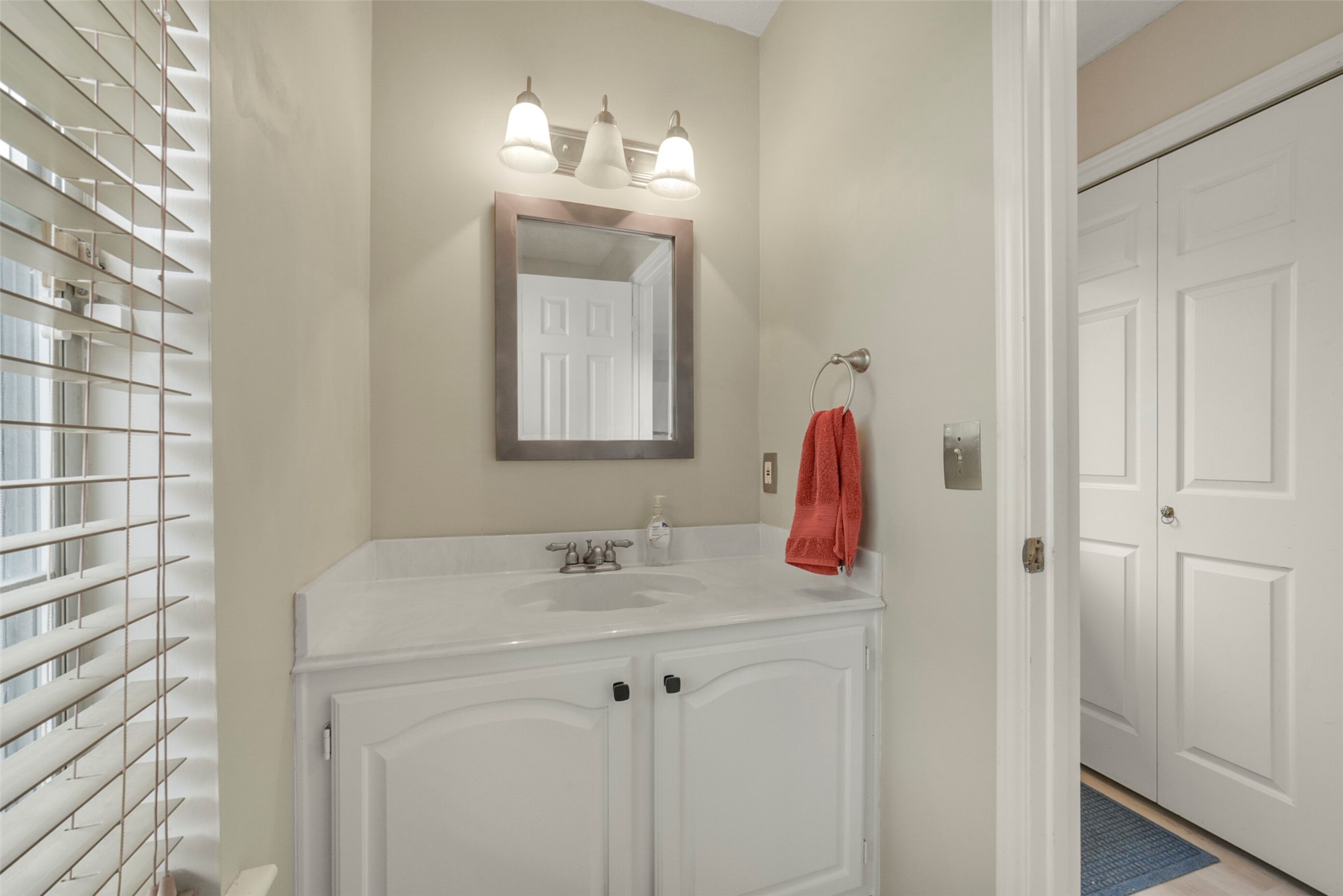 10410 Dude Road Houston, TX 77064 - Photo 14 of 45 This bathroom features a clean, modern design with a white vanity, a sleek countertop, and a large mirror. It is well-lit with two stylish light fixtures and includes a towel holder. The space has neutral walls and a window with blinds, offering a bright and inviting atmosphere.