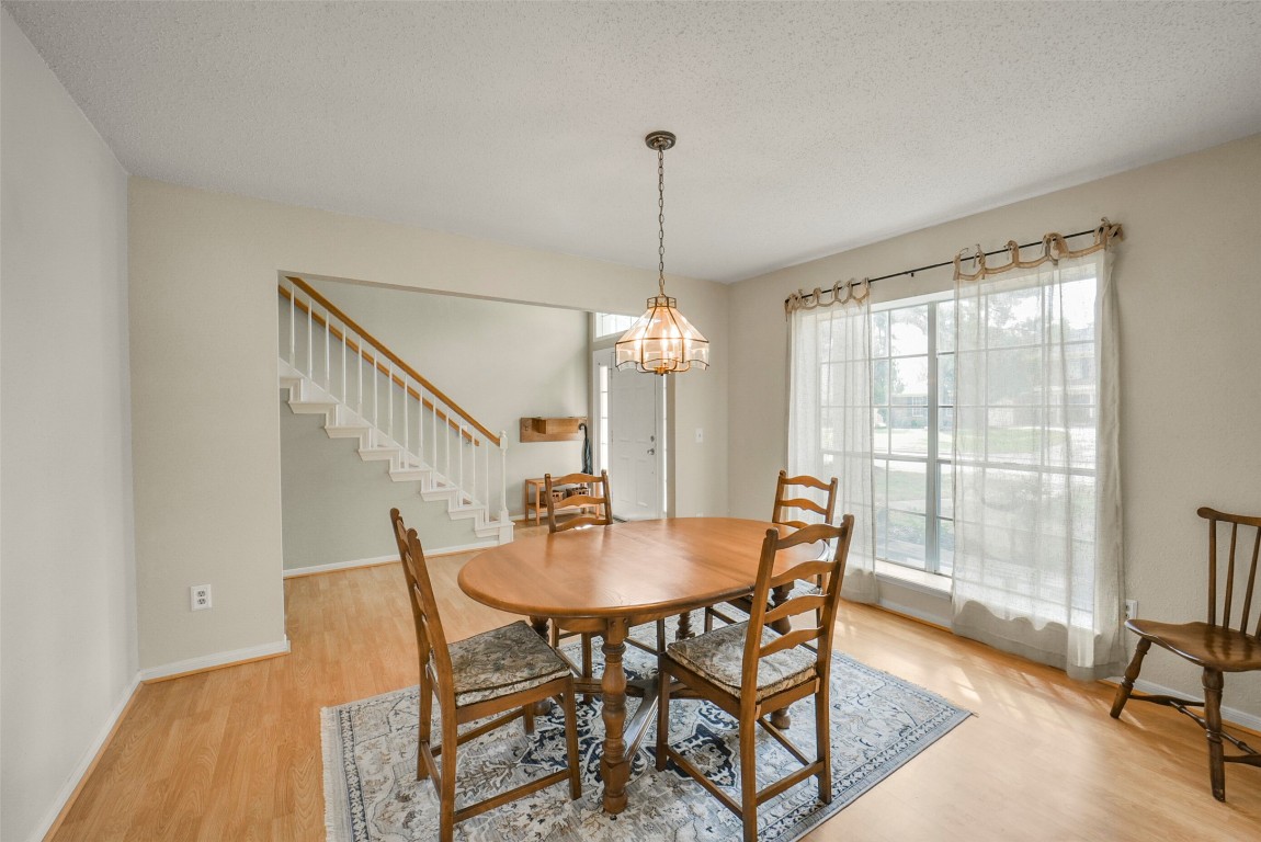10410 Dude Road Houston, TX 77064 - Photo 15 of 45 This bright dining area features wood flooring and a large window that lets in natural light. It includes a cozy wooden dining set and a stylish pendant light. The space opens to a staircase, creating an inviting and connected atmosphere.