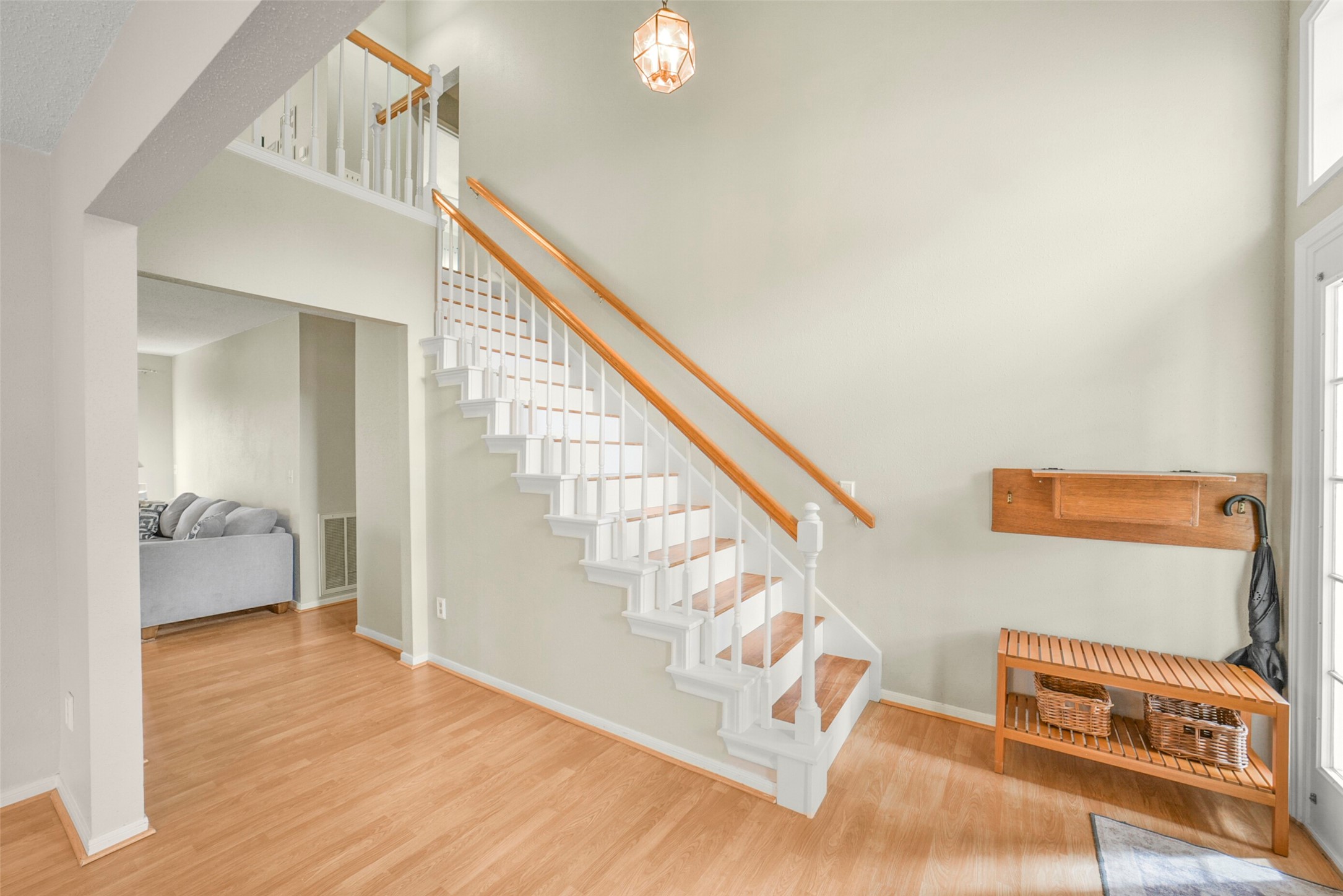 10410 Dude Road Houston, TX 77064 - Photo 17 of 45 This inviting foyer features a bright, open staircase with wooden railings and white balusters, complemented by light wood flooring. A nearby entryway bench with storage offers practicality, while a hanging light fixture adds a warm touch. The space seamlessly leads into a cozy living area.