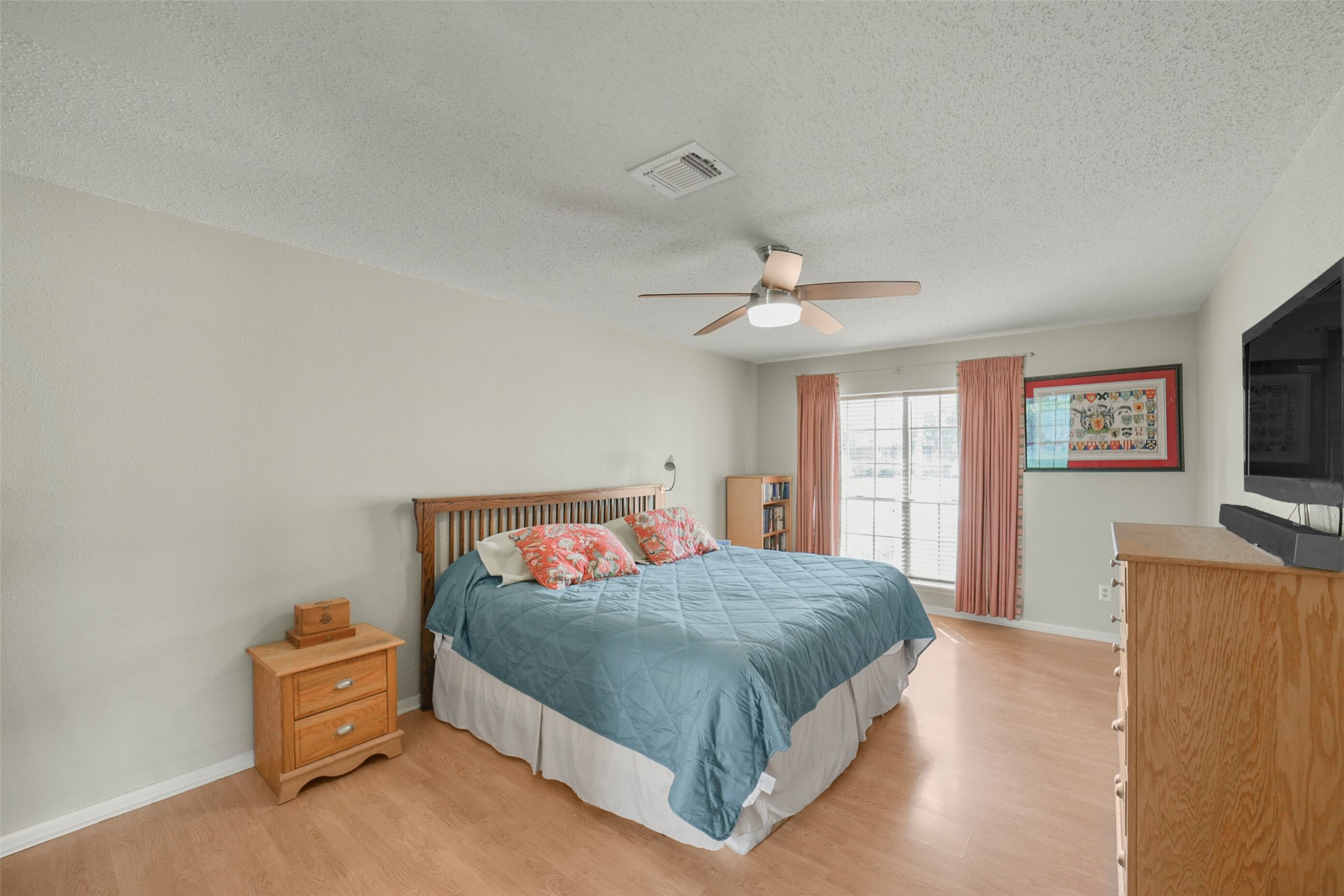 10410 Dude Road Houston, TX 77064 - Photo 18 of 45 Bright, spacious bedroom with wood flooring, featuring a cozy bed, ceiling fan, and large window for natural light. Includes a dresser, nightstand, and wall-mounted TV.