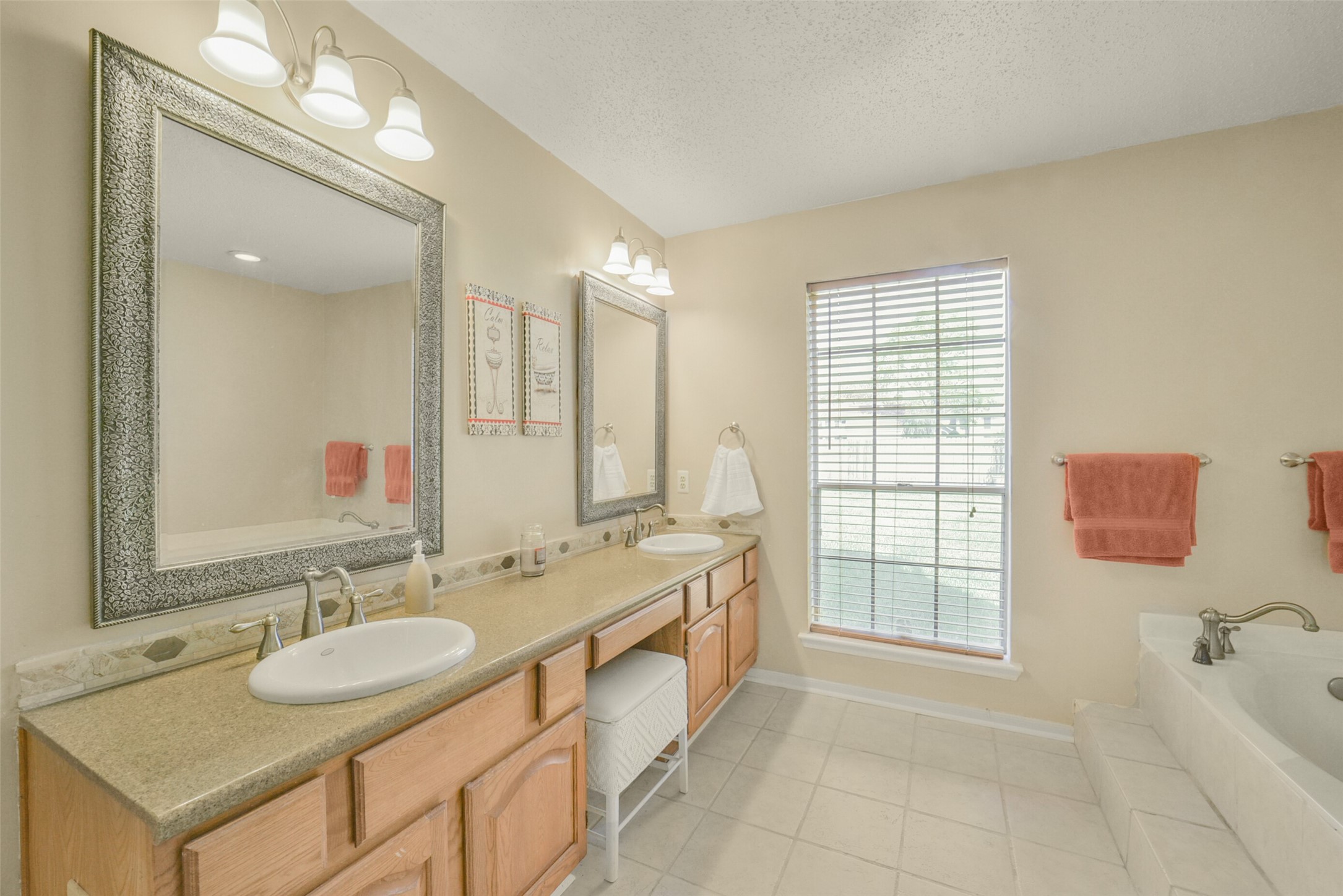 10410 Dude Road Houston, TX 77064 - Photo 20 of 45 This bathroom features a double vanity with elegant framed mirrors, ample cabinetry, and modern light fixtures. It has a large window for natural light and a spacious tub, providing a bright and inviting atmosphere.