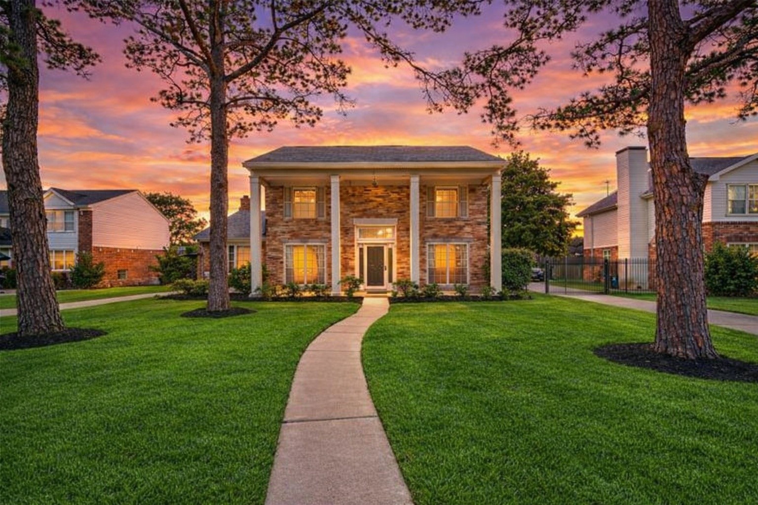 10410 Dude Road Houston, TX 77064 - Photo 2 of 45 This photo showcases a charming two-story brick home with classic columns, set against a stunning sunset backdrop. It features a well-manicured lawn, a welcoming front path, and mature trees, creating an inviting and picturesque curb appeal.
